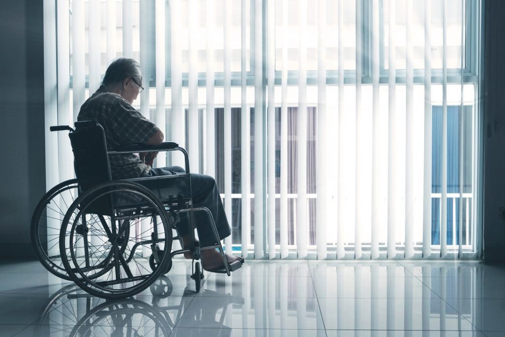 Elderly man in wheelchair looking out from nursing facility window